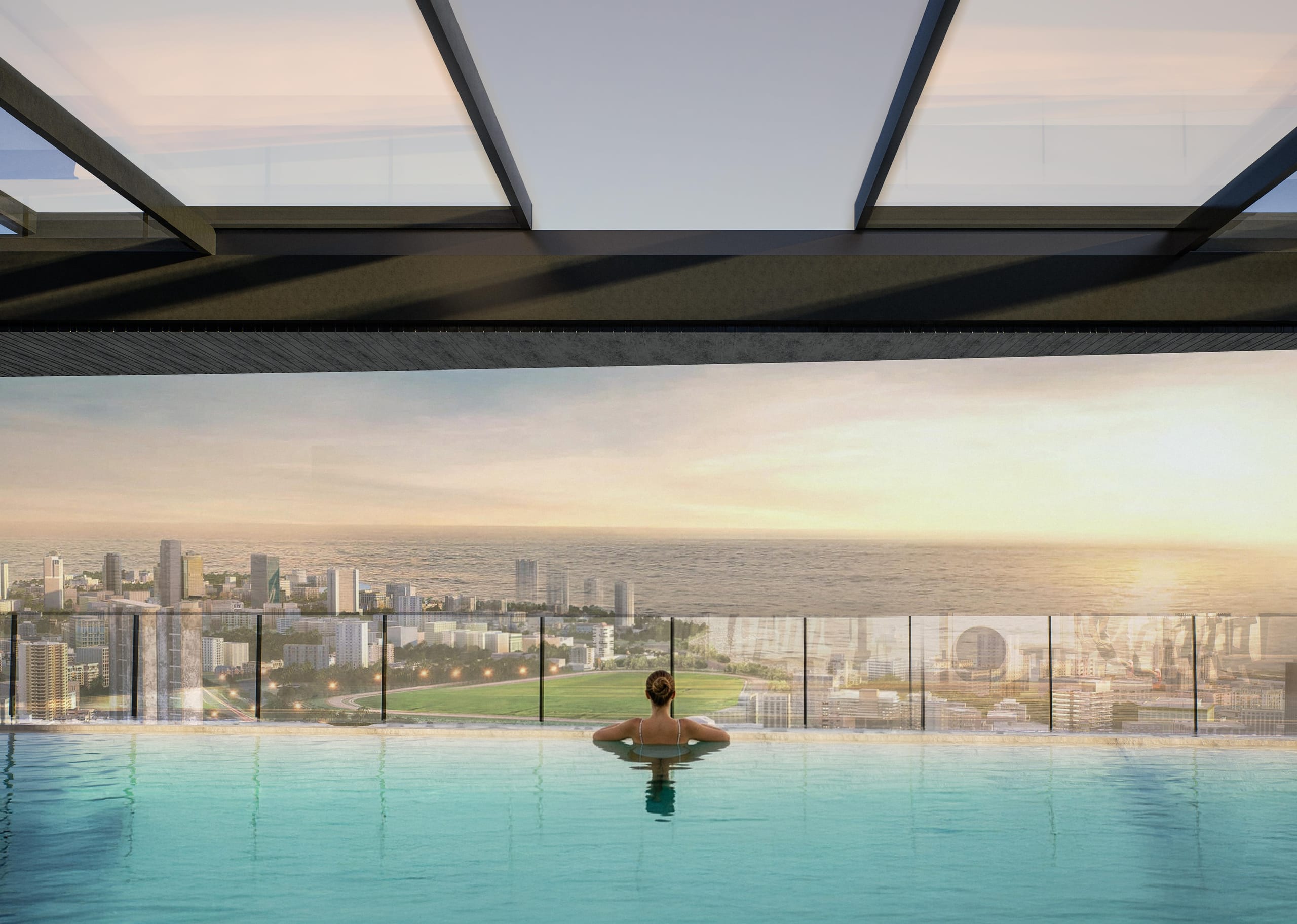 A woman resting at the edge of the infinity pool under the steel and glass canopy, looking out over the city and the sea at sunset.