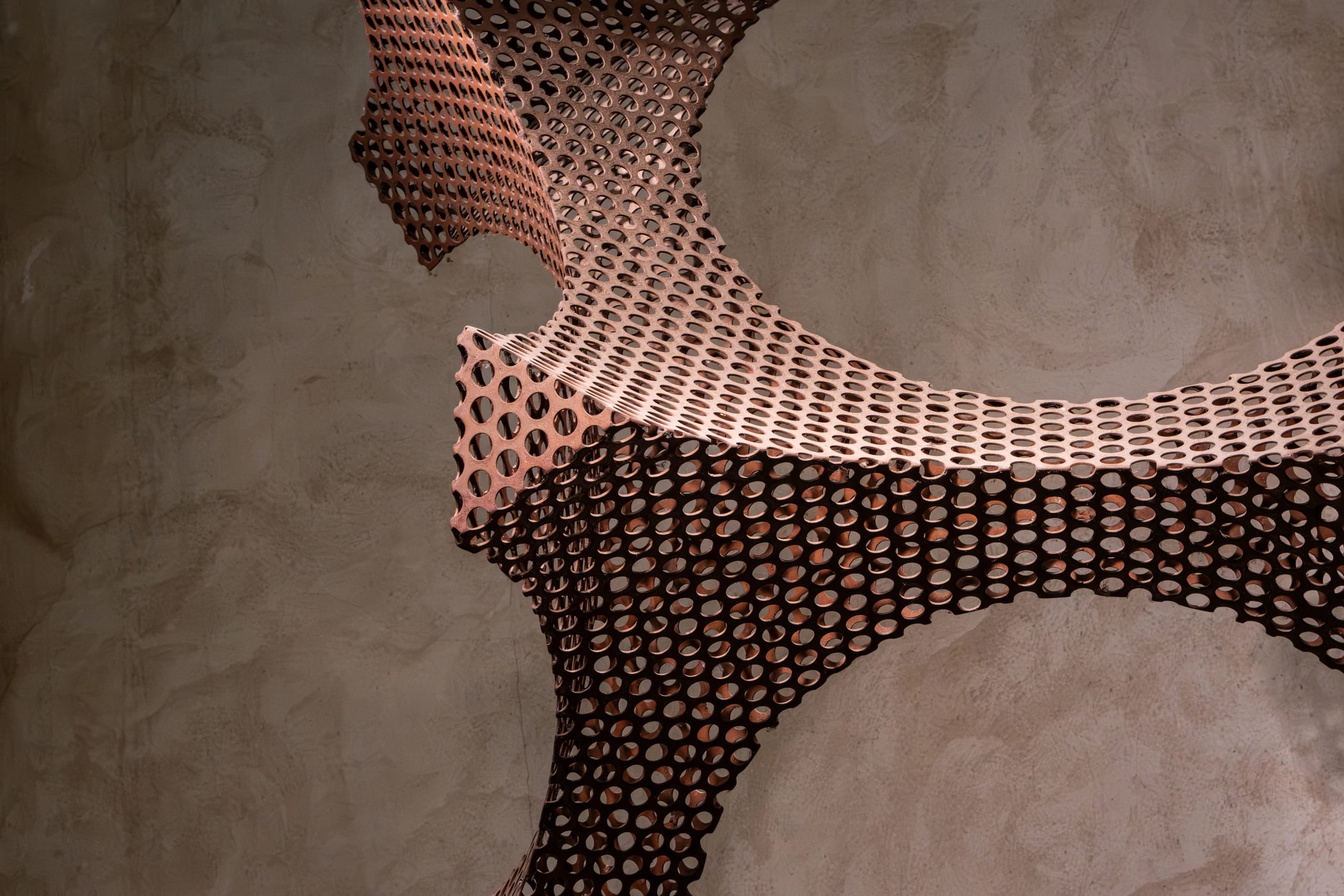 Perforated metal sculpture casting shadows on a textured wall