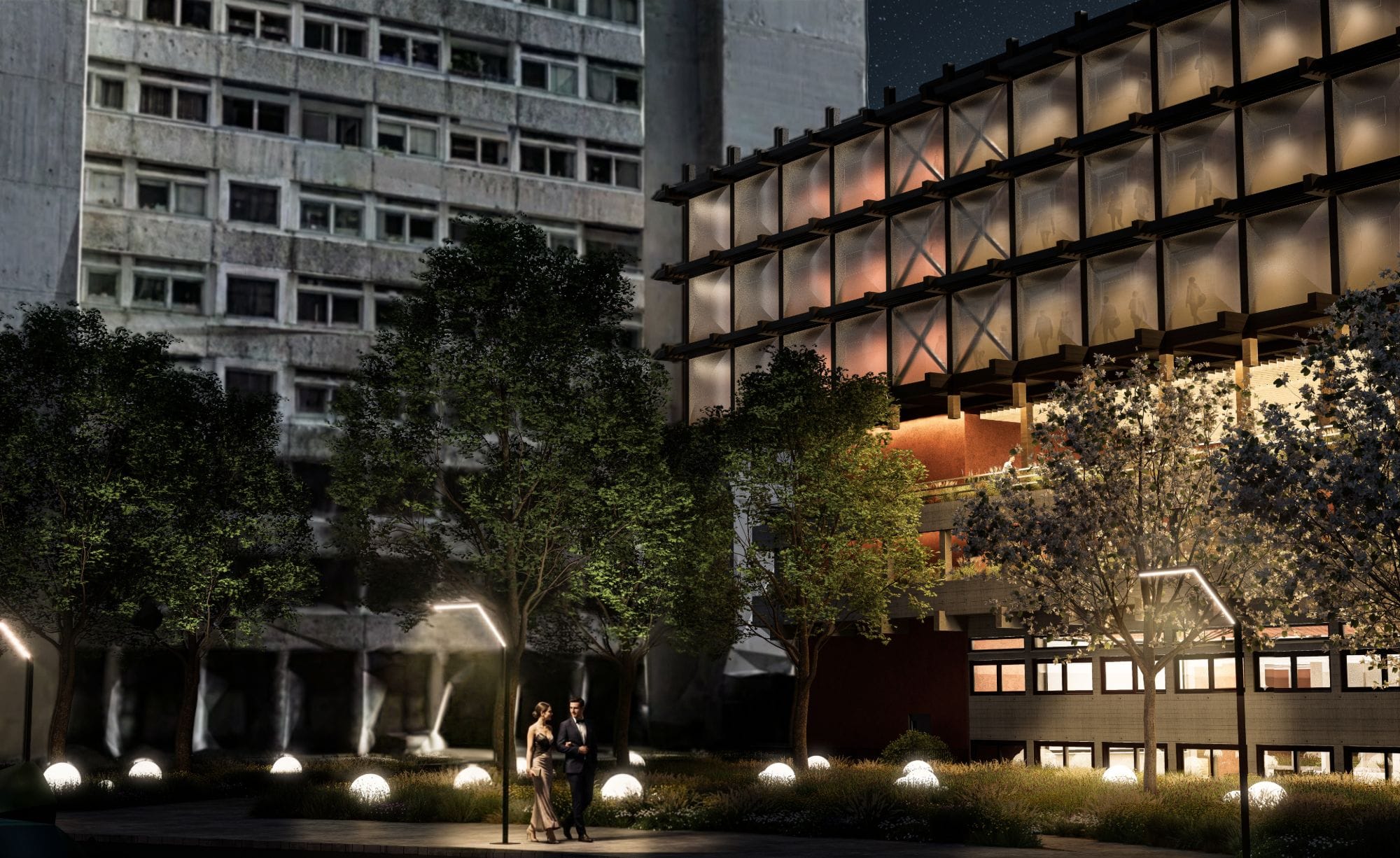 Night view of a couple walking through the planted courtyard with glowing sphere lights, beside the illuminated ETFE facade and a concrete housing block.