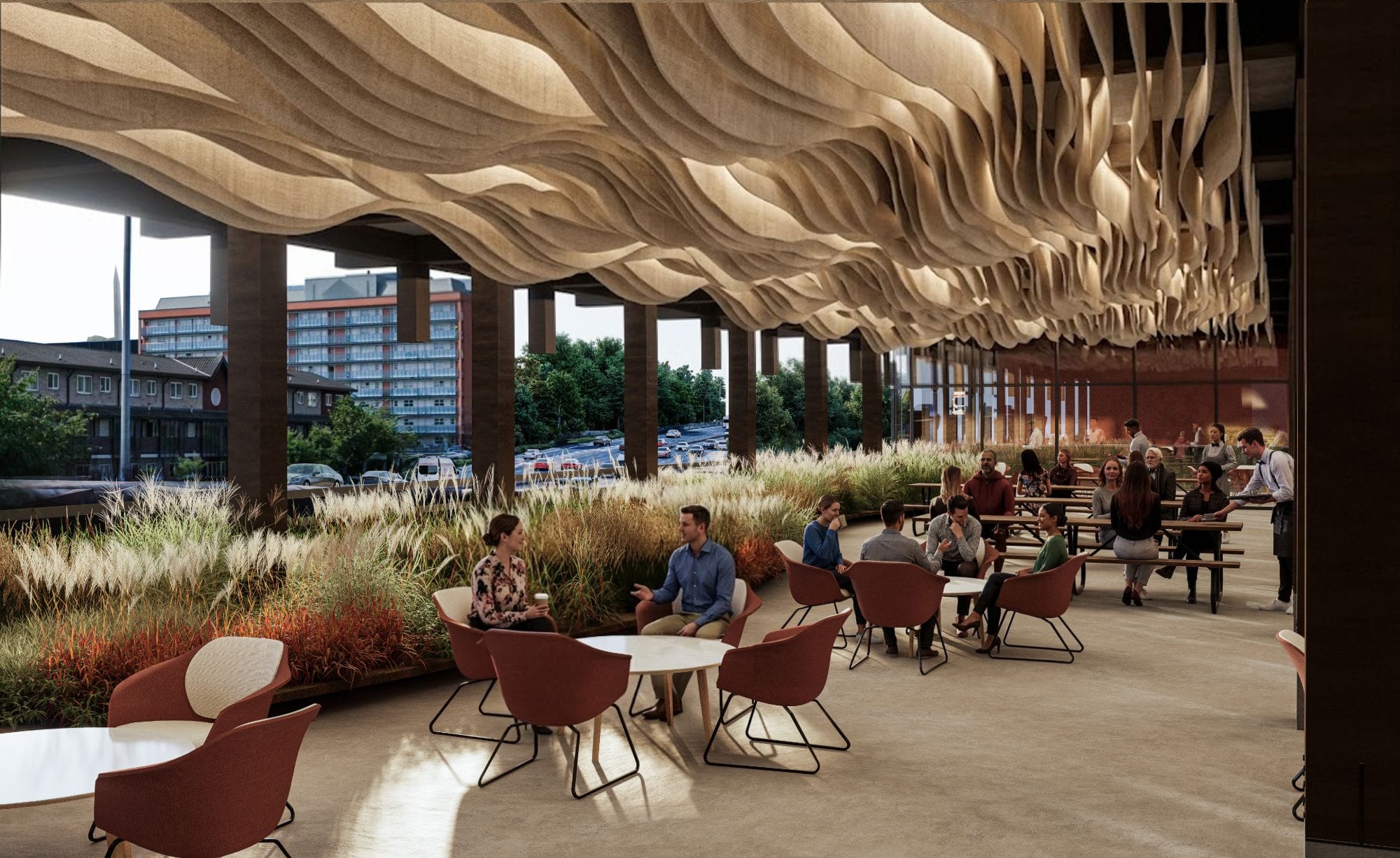 Rooftop café terrace with people at tables under a draped wave-like textile ceiling, framed by planted grasses and a view over the Mancunian Way.