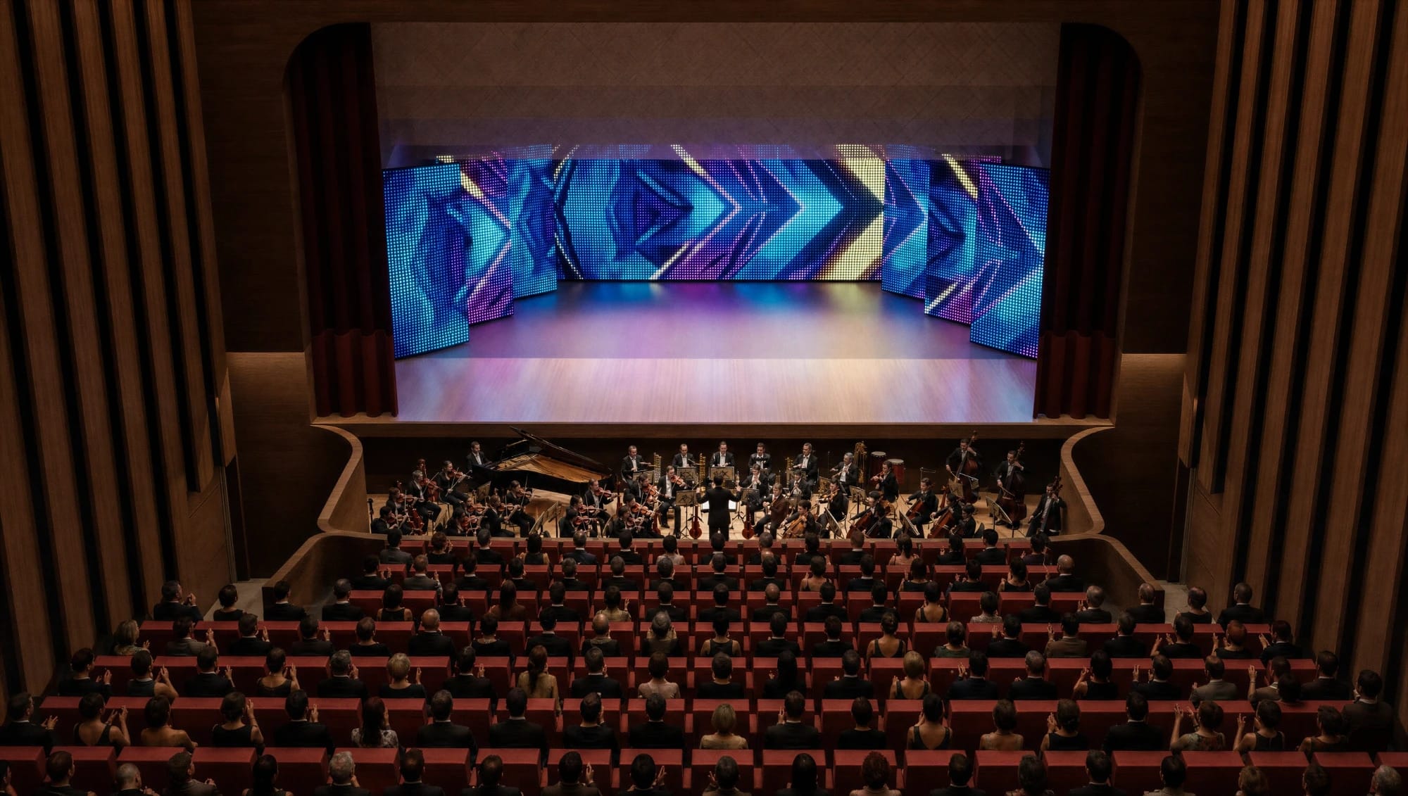 View from the balcony of a full auditorium applauding an orchestra in the pit, with LED screens lighting the stage in blue and purple.