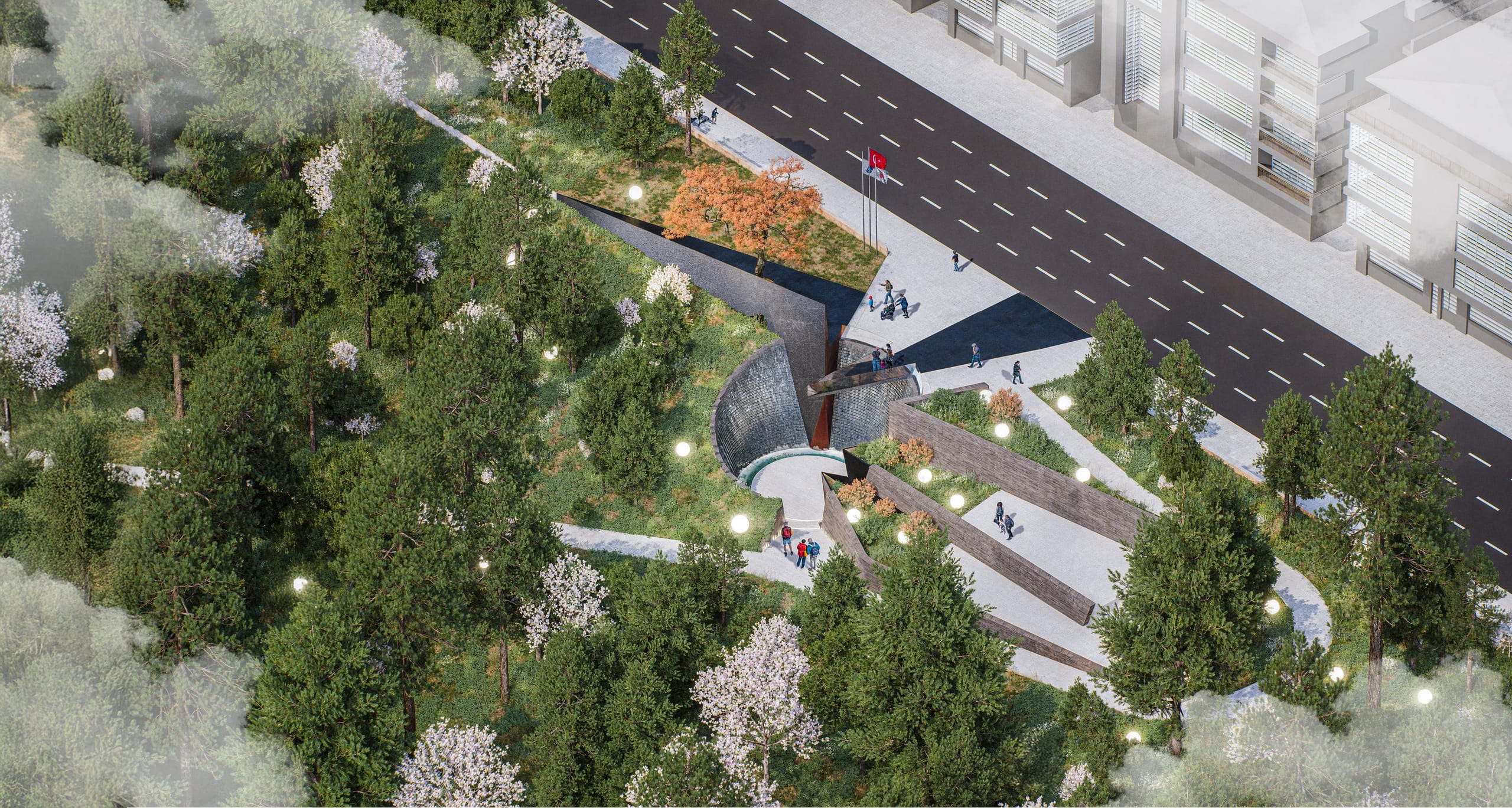 Aerial view of the memorial set into the wooded slope of the Botanic Park beside Çankaya Street, with the circular granite void, the dark angled memorial wall with flags and an orange-leaved tree, terraced planting and sphere lights.