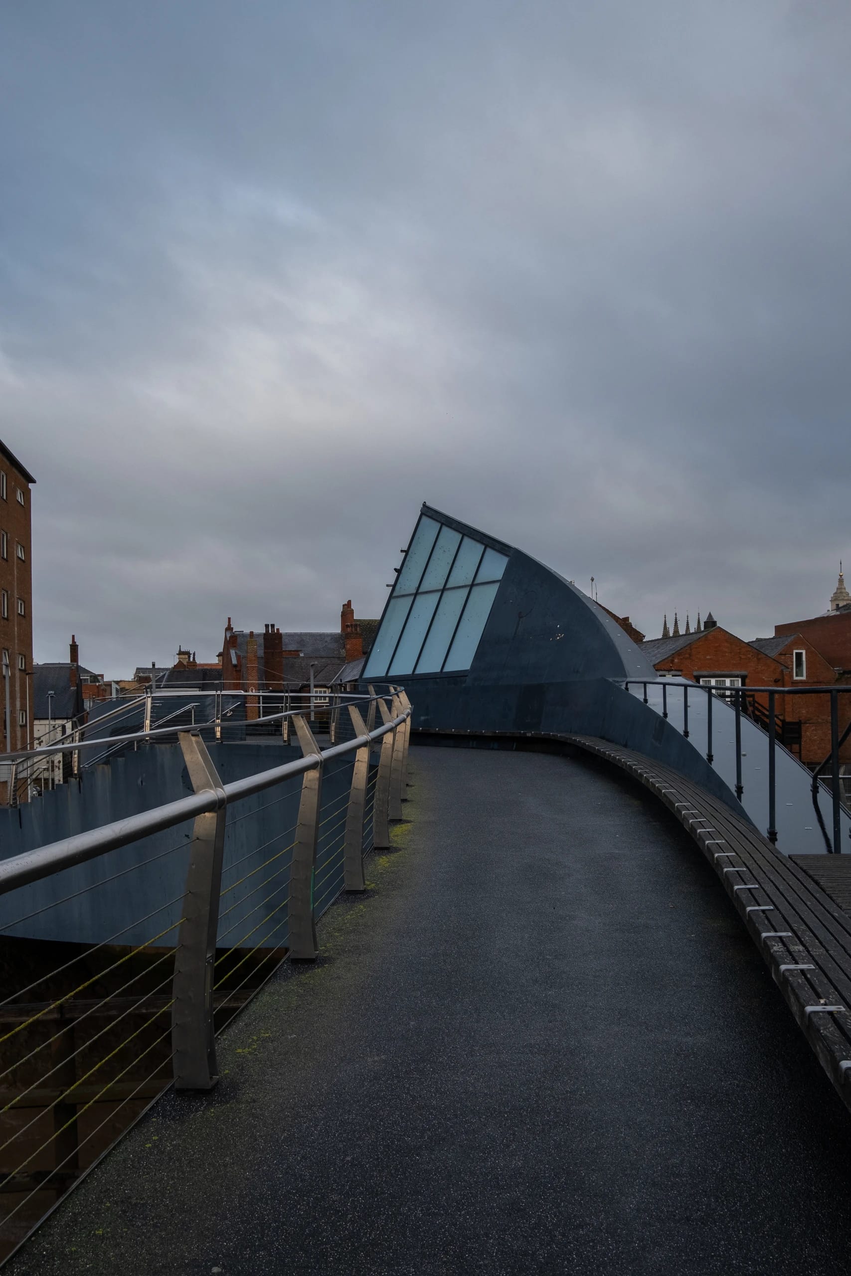 A curved elevated walkway leading towards an angular glazed structure