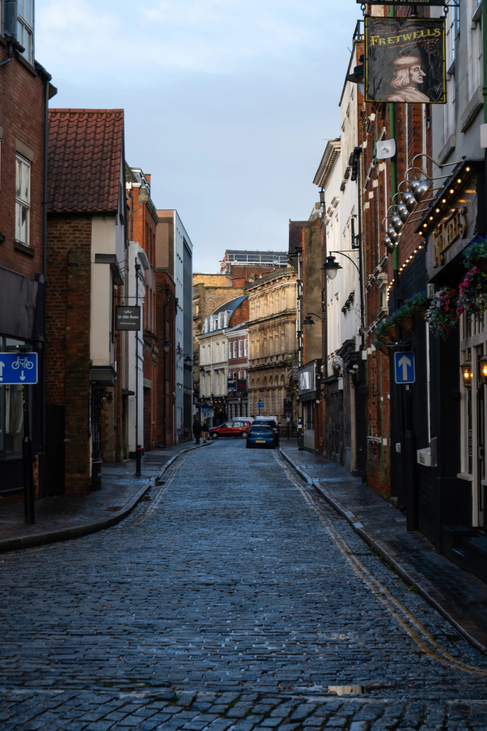 A cobbled street lined with historic buildings and hanging pub signs
