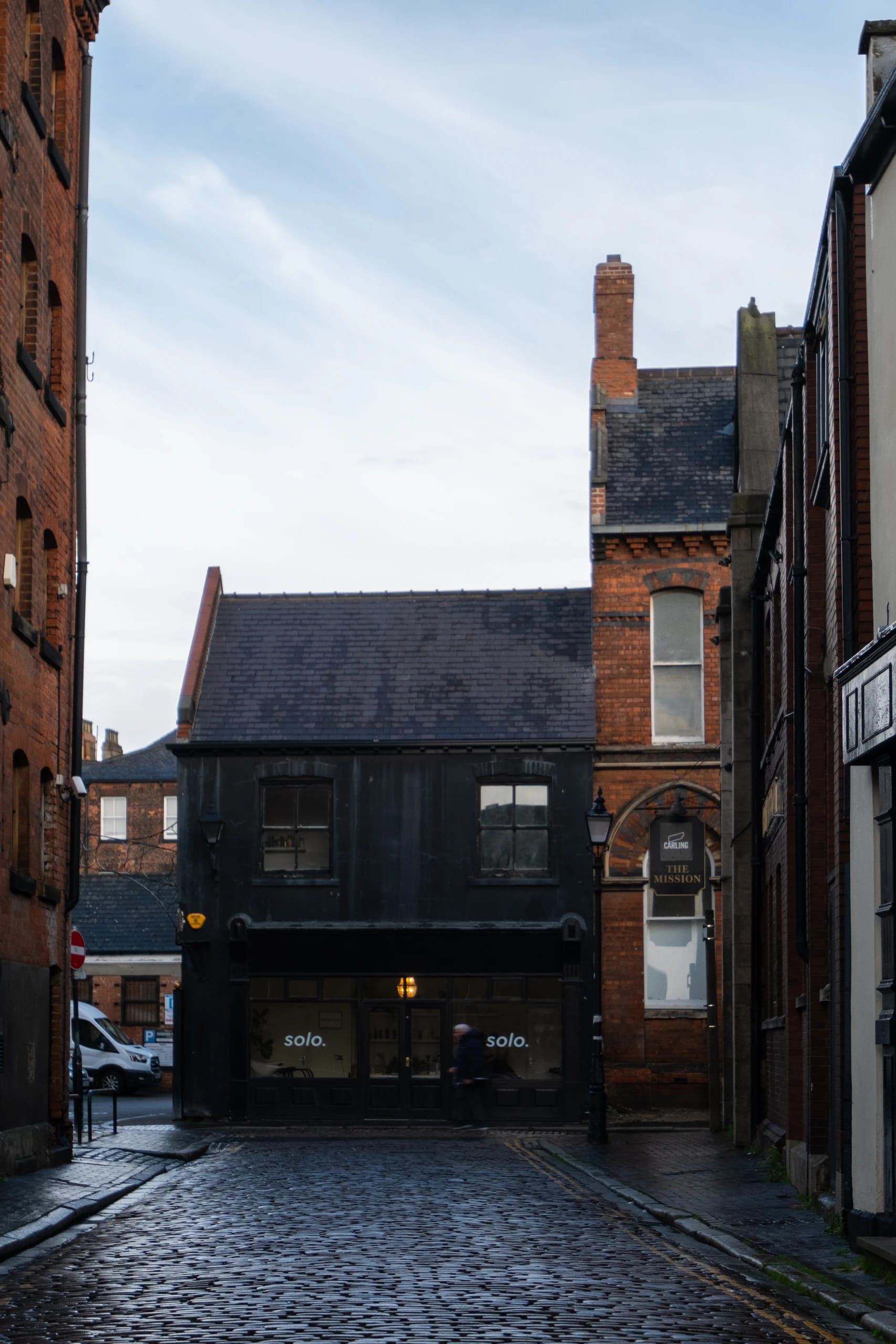 Historic brick buildings and a dark shopfront at the end of a narrow street