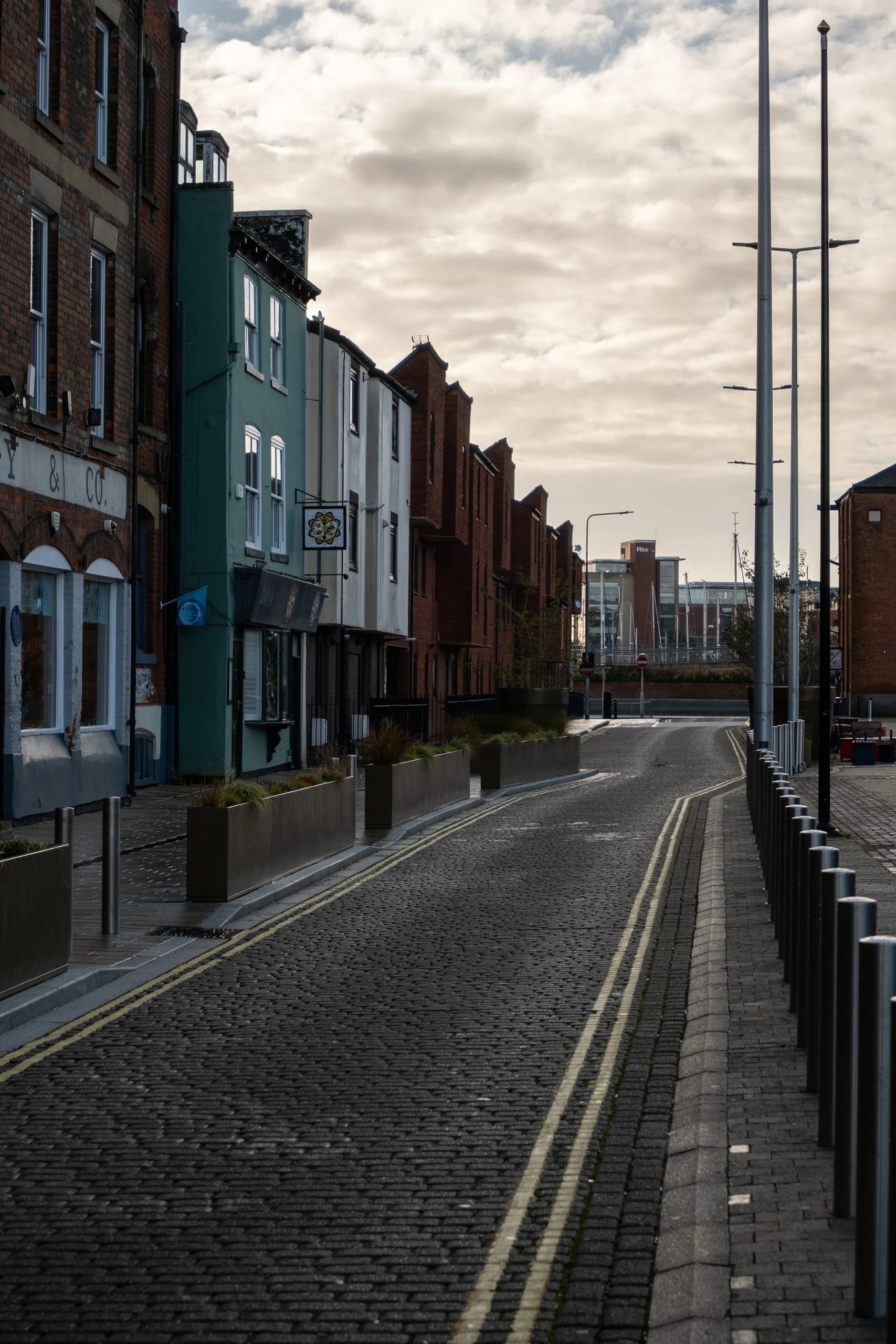 A cobbled waterfront street lined with brick buildings and planters