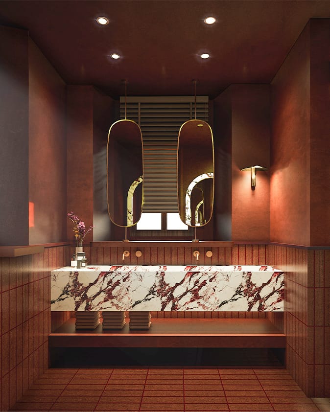 Terracotta-toned washroom with a red-veined marble double basin, two oval brass-framed mirrors hung in front of a window and wall-mounted brass taps.