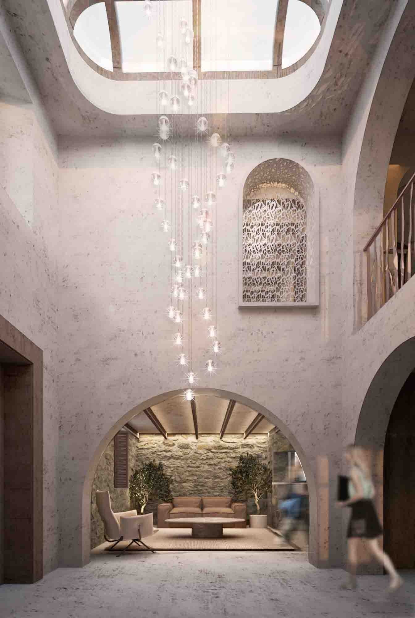 The double-height atrium under an oval skylight, with a cascade of glass pendant lights, a perforated arched niche, a gallery above and an arched opening to the stone-walled lounge.