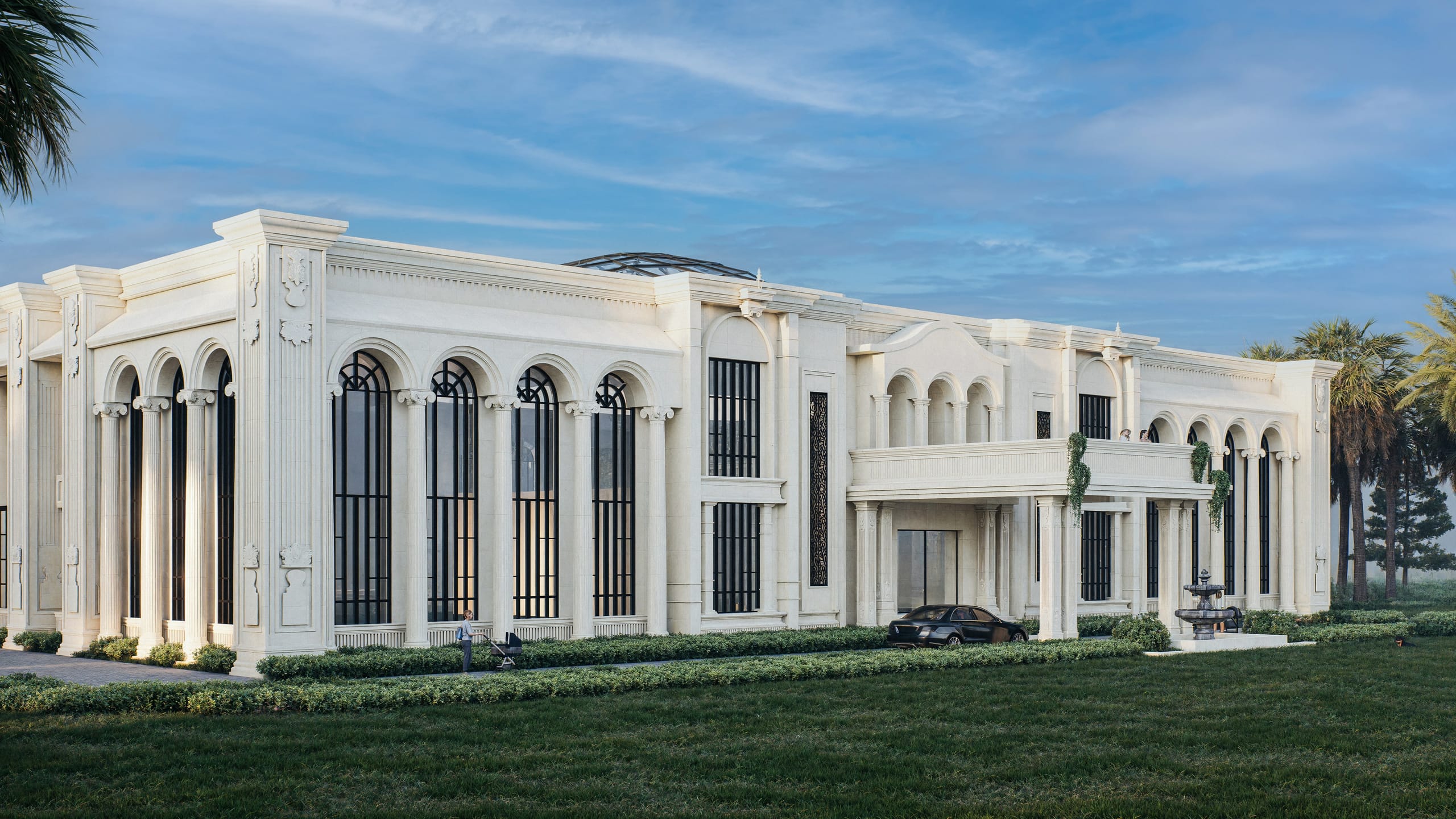 Corner view of the white villa with columned arched windows, the entrance porch with a balcony above, a fountain and a parked car, under a blue sky.