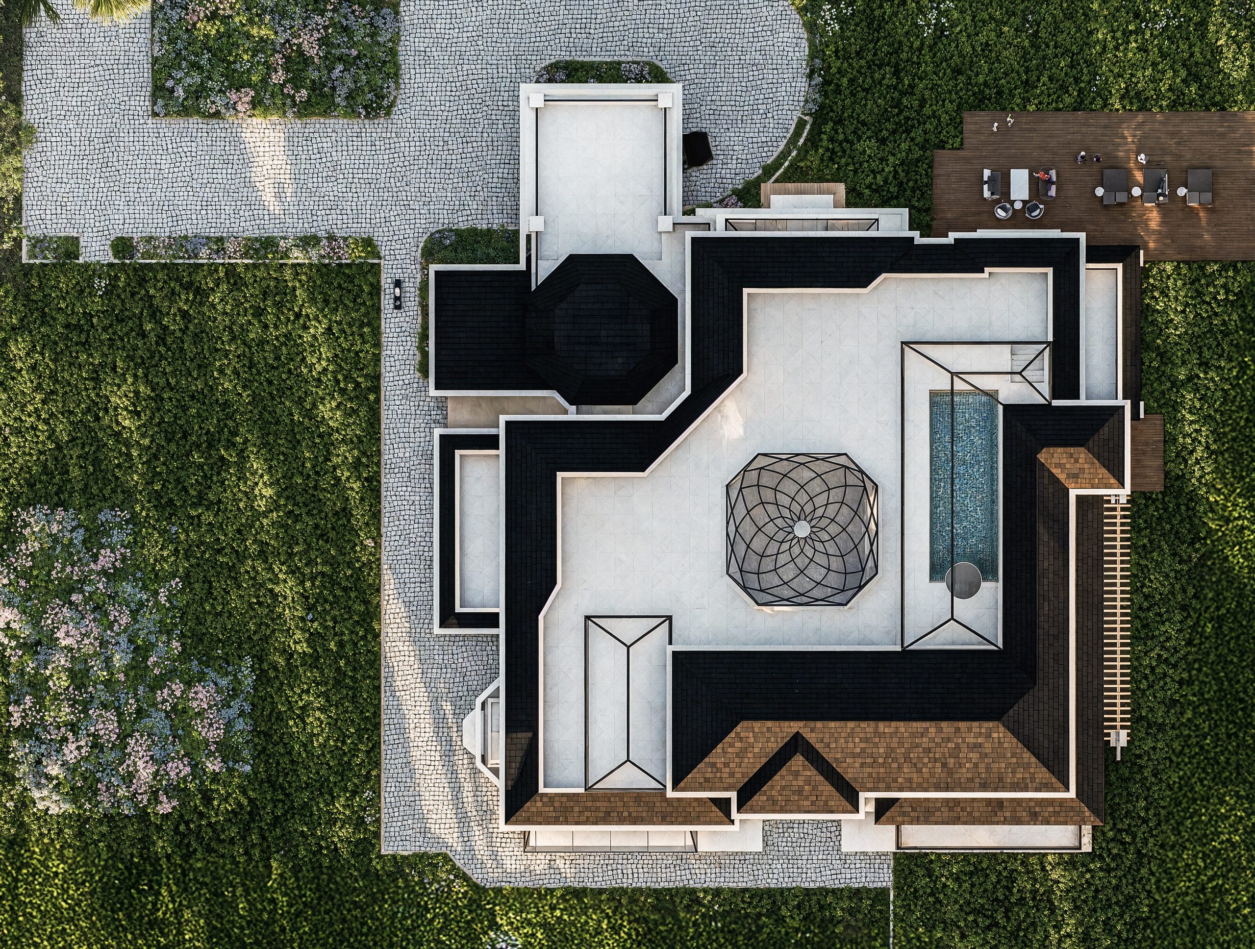 Top-down view of the villa's roof terrace, with the round faceted glass dome at the centre, a long rooftop pool, glazed lanterns, dark slate roofs and the cobbled drive and gardens around.