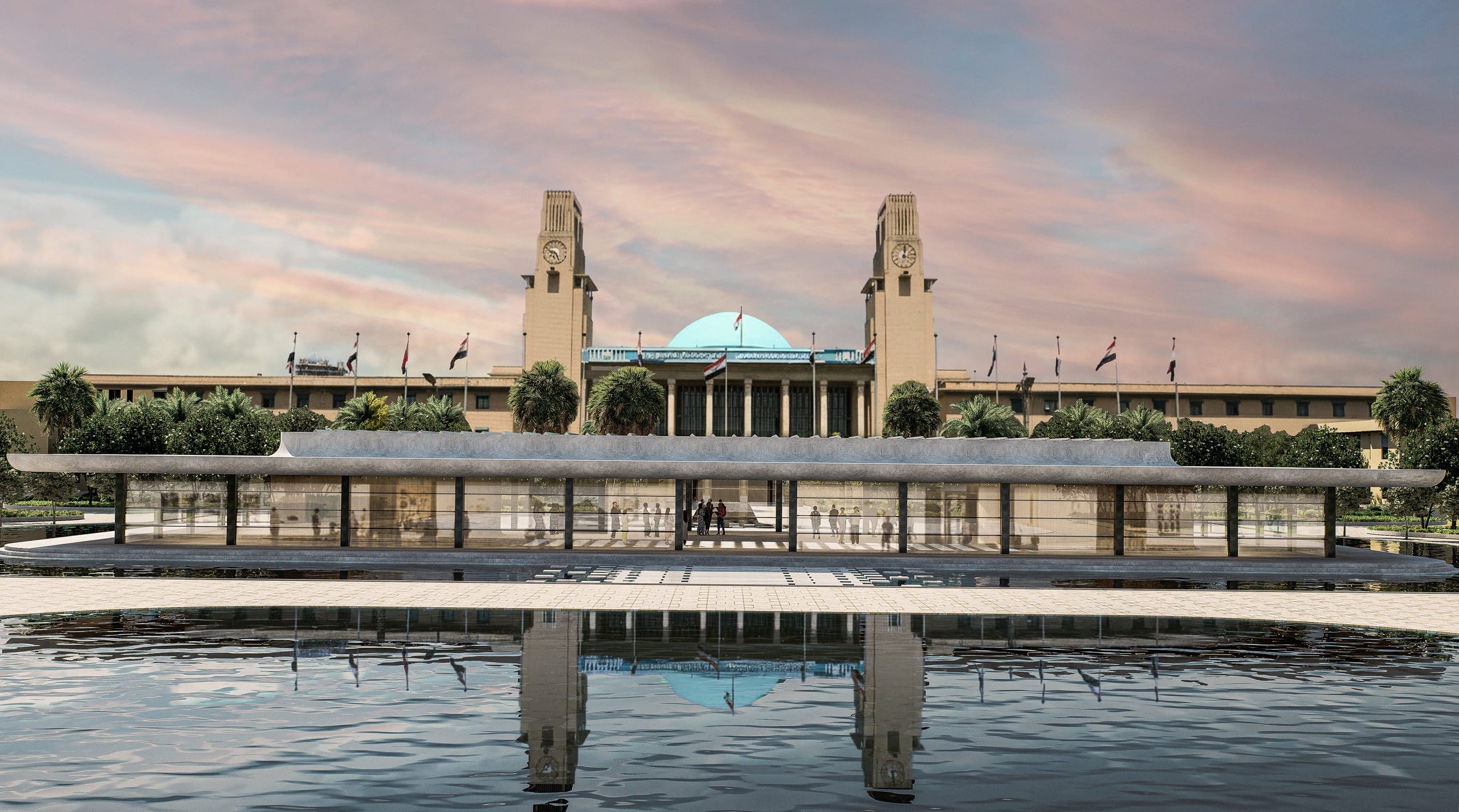 Frontal dusk view of the long, low exhibition pavilion reflected in the pool in front of Baghdad Central Station, with its two clock towers, green dome and flags behind.