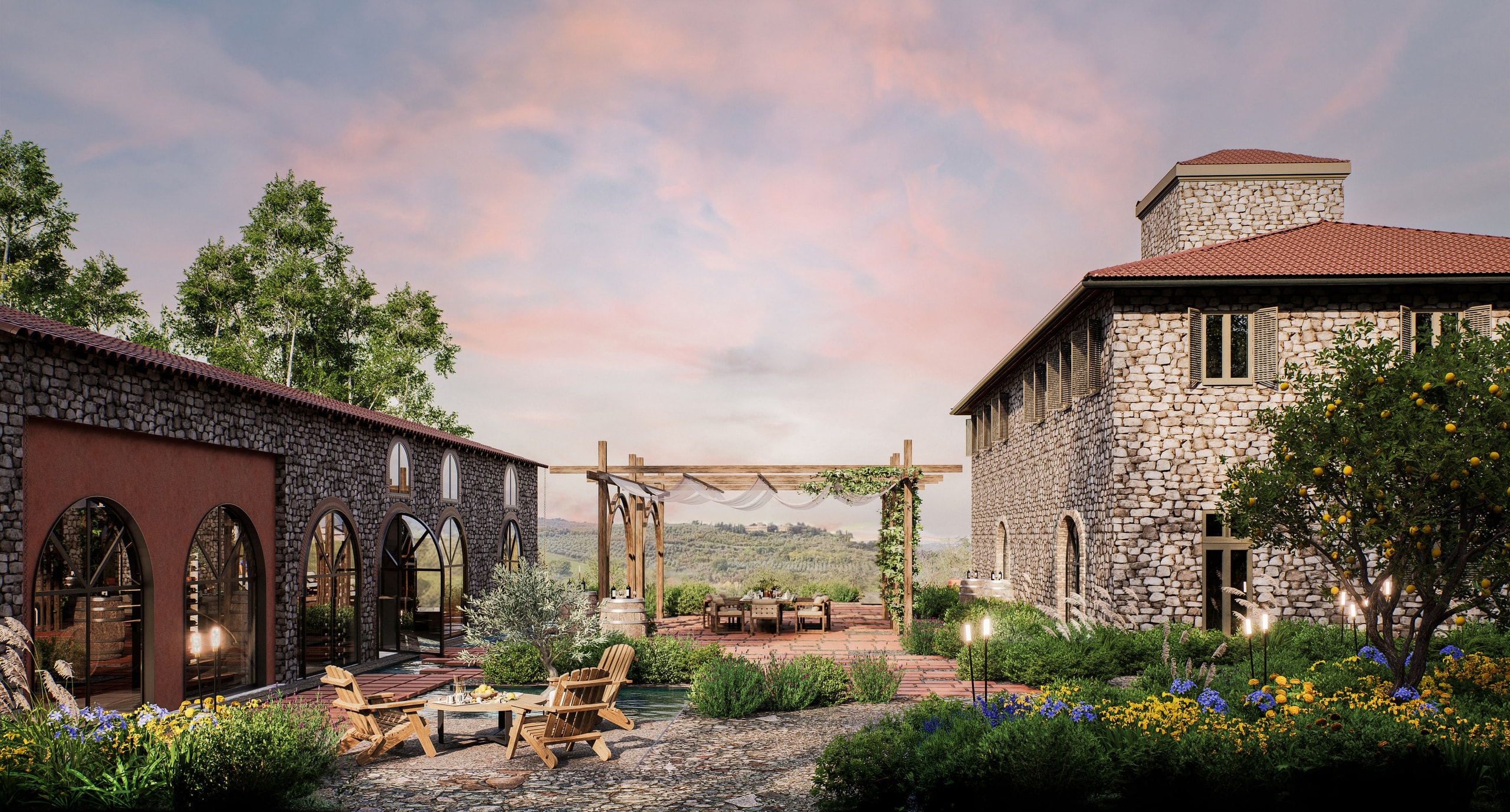 Courtyard of a Tuscan stone estate at sunset, with the arched winery on the left, the manor house on the right, a pergola and dining table framing the vineyard hills, and wooden chairs around a fire table among flowering planting