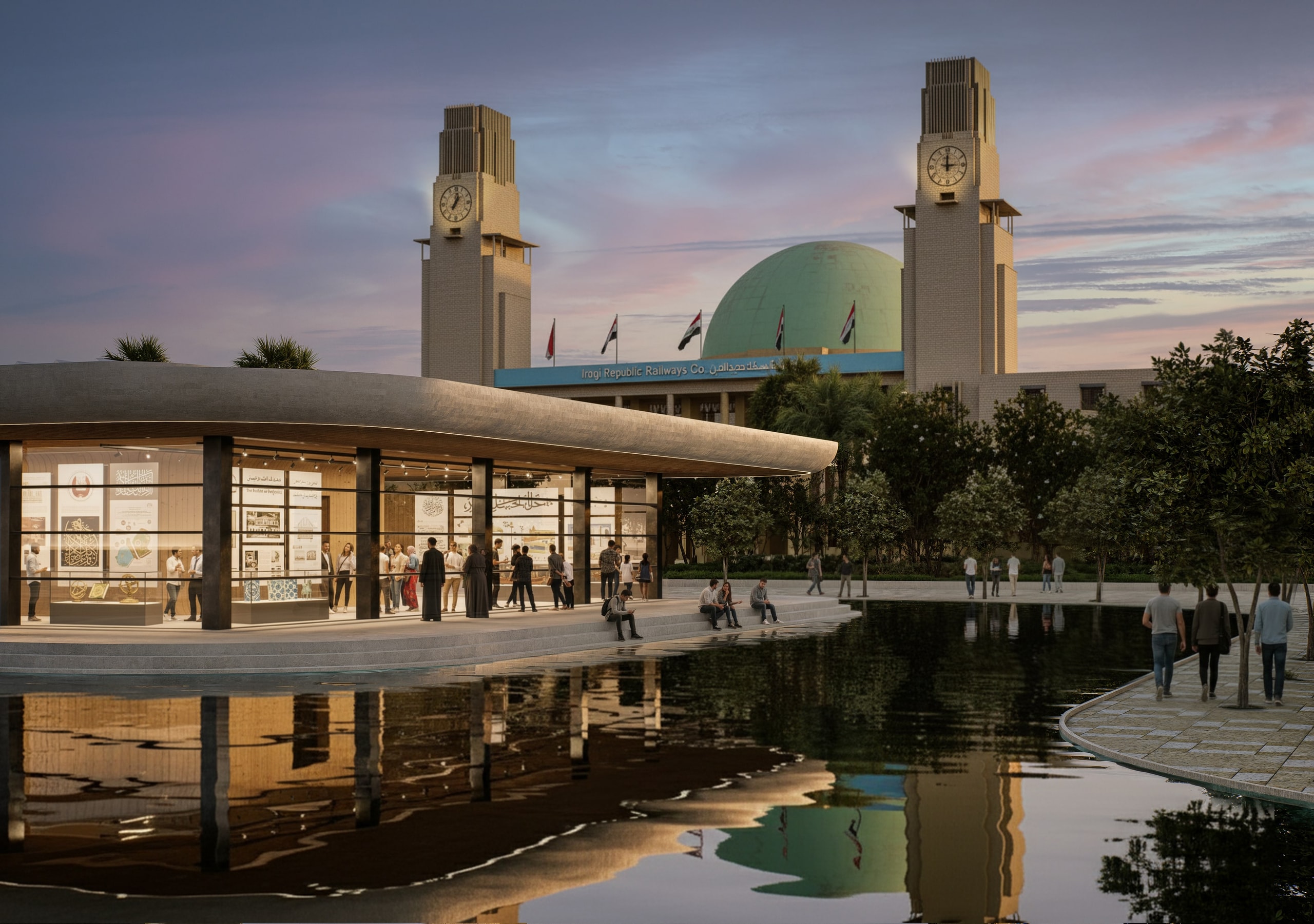 Dusk view of a glass exhibition pavilion with a curved roof beside a reflecting pool, with people gathered inside and along the water, in front of the clock towers and green dome of Baghdad Central Station